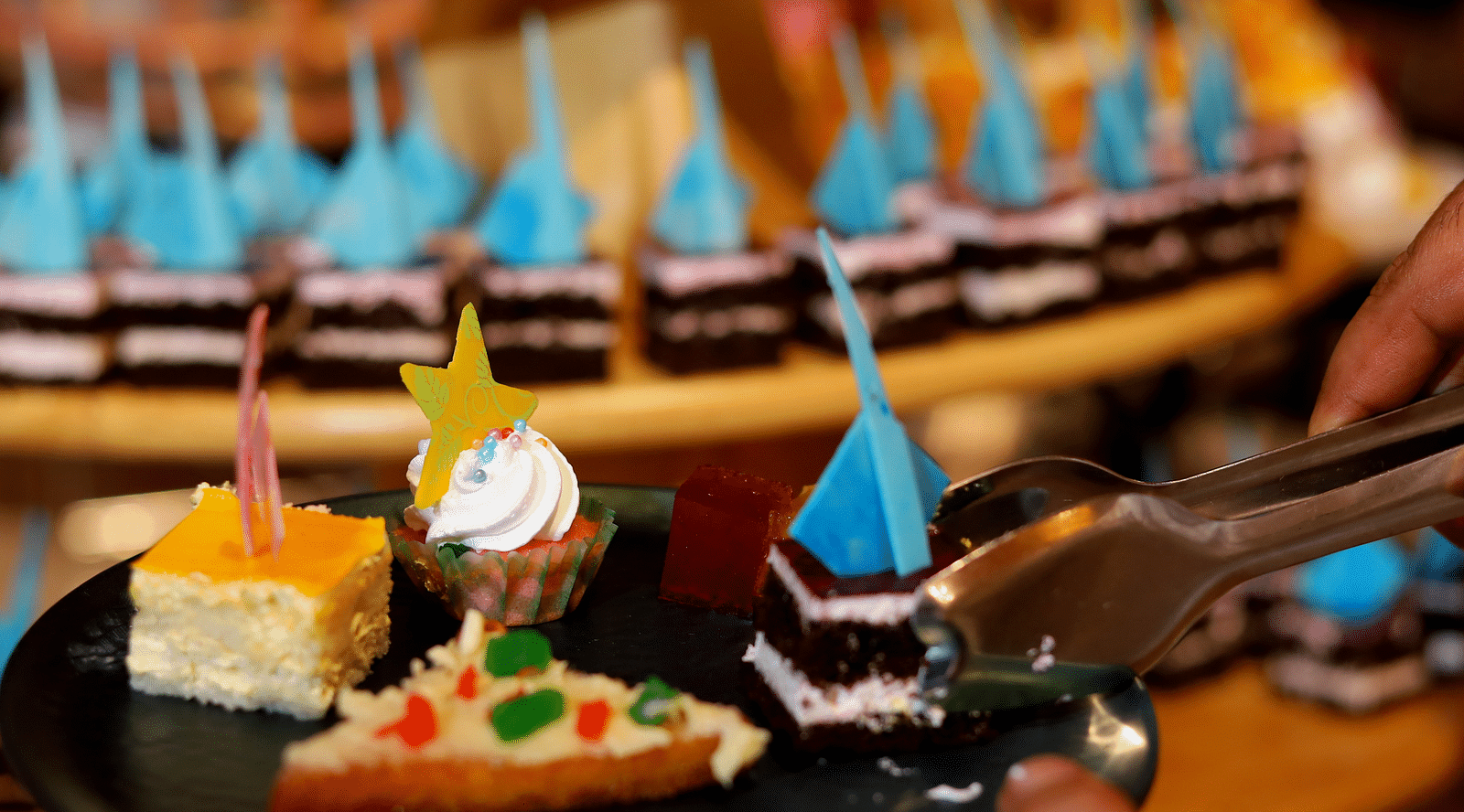 A serving platter featuring a slice of colorful pizza and assorted desserts with a birthday candle Themis Barbecue House, Ambience Mall, Gurugram
