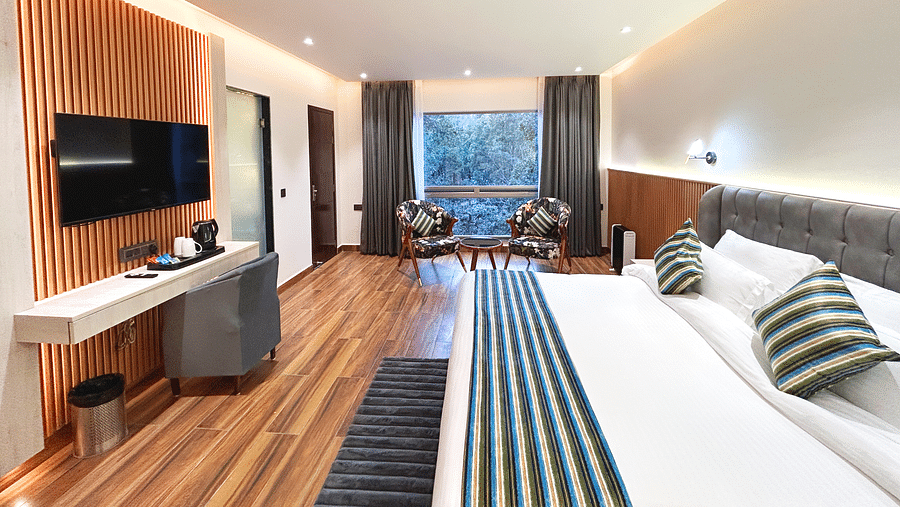 An image of the premium room at DLS The Emerald, Nainital featuring a bed, a flat screen TV, chairs and table and a window overlooking the view