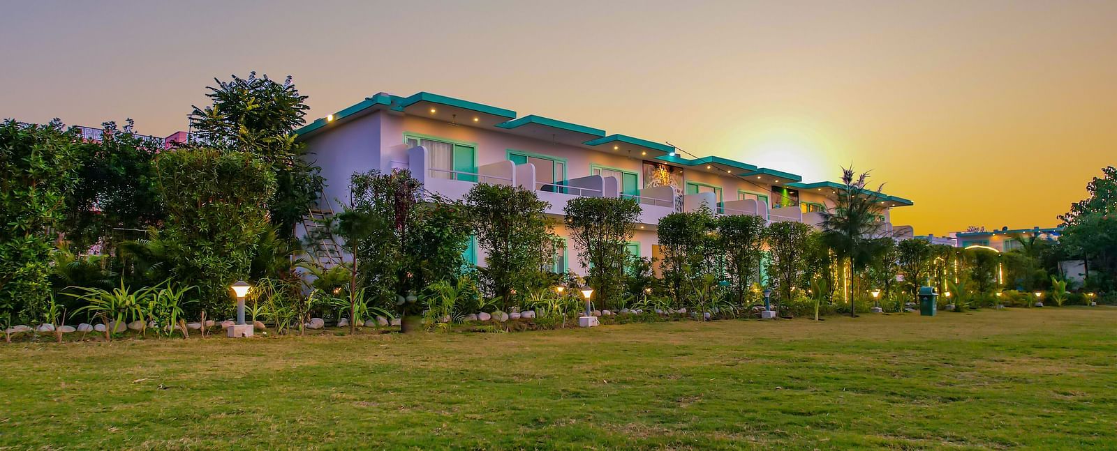 The exterior of Vedikant Resorts The Mallard Corbett is seen at dusk with lights illuminating the buildings and grounds.