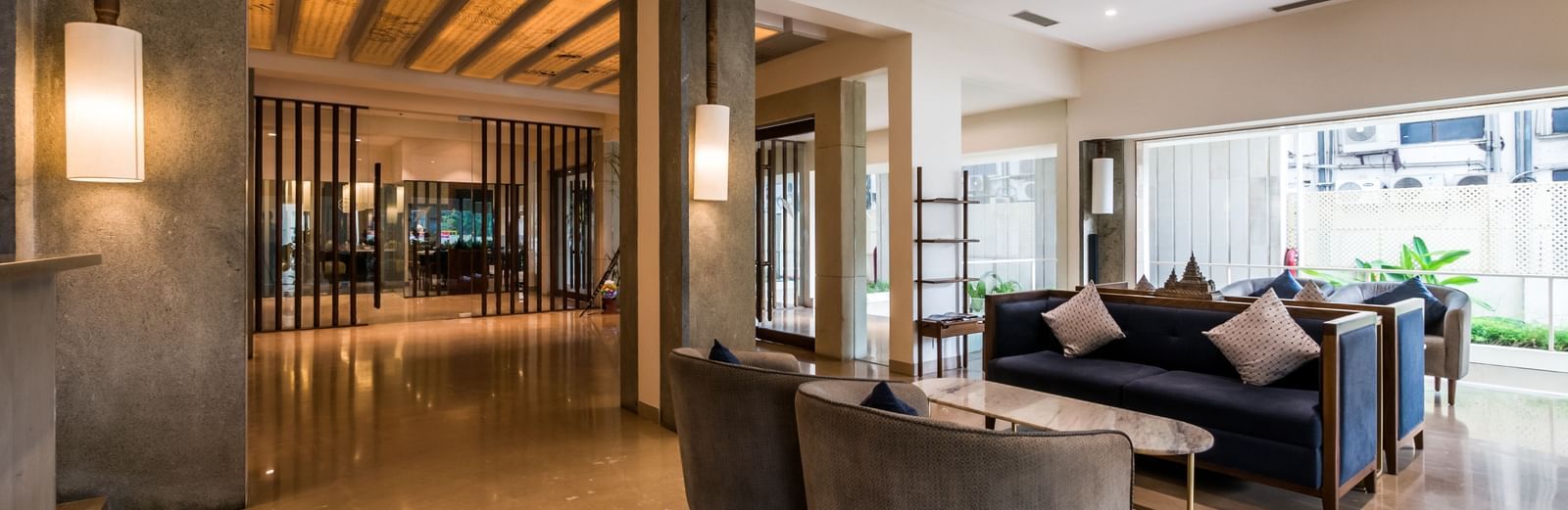 A lounge area featuring comfortable chairs, a marble-top sofa, soft lighting, and sliding glass doors leading deeper into the reception space.