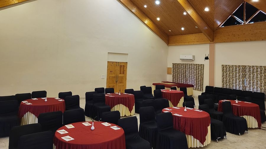 A spacious banquet hall with high wooden ceilings, elegant lighting, and round tables set for events at Dagshai Manor Kasauli - Inde Hotels.