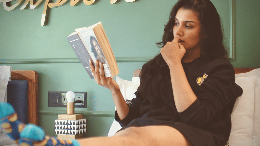 Guest relaxing on a cosy bed at Theory9 Premium Service Apartments, Bandra, reading a book in a modern room with warm lighting and contemporary decor.