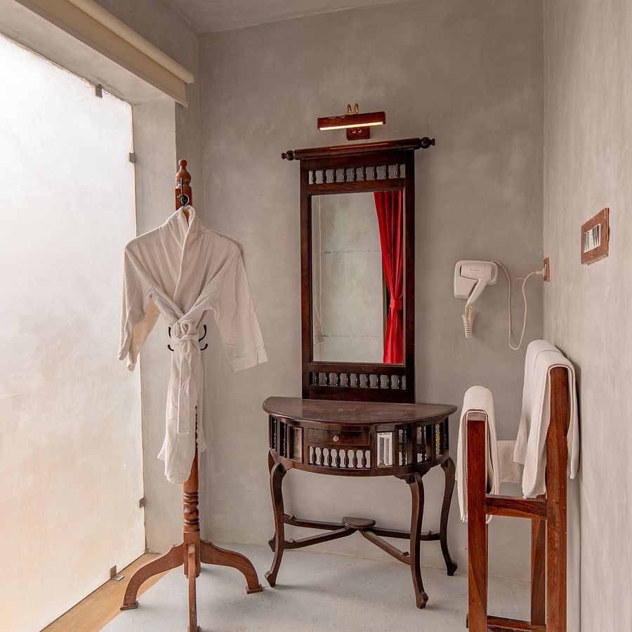alt-text An image of a room section with mirror on the wall, below it a dressing table is placed, next to it there is a bathrobe hanged - Karwaan Jaisalmer