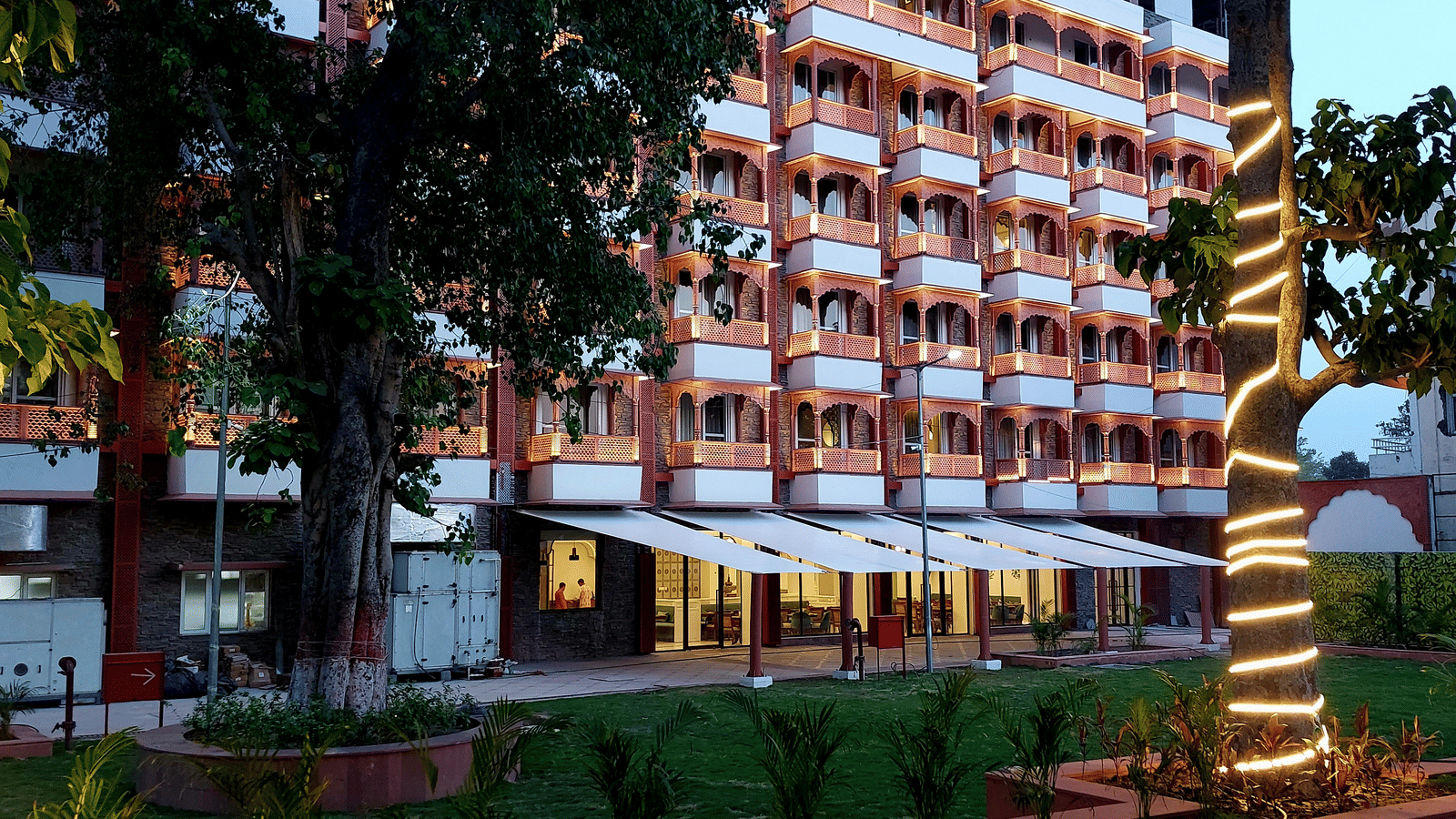 Facade of Bhagirathi by Atishay amid trees with their trunks glowing with warm string lights