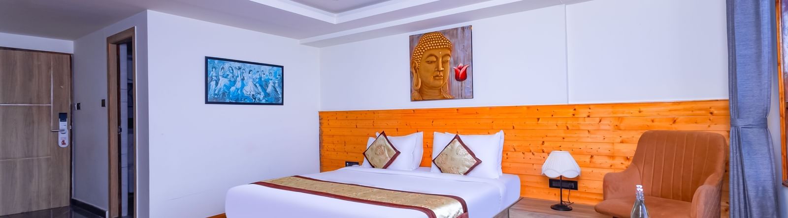 Elegant bedroom at Sumitel Premier Inn, Siliguri, featuring a cosy bed, soft lighting, wooden interiors, and seating chairs creating a warm and welcoming stay.
