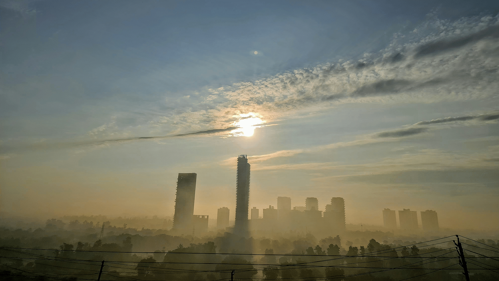 An overview of the city of Gurgaon with the sun just above a high rise building.