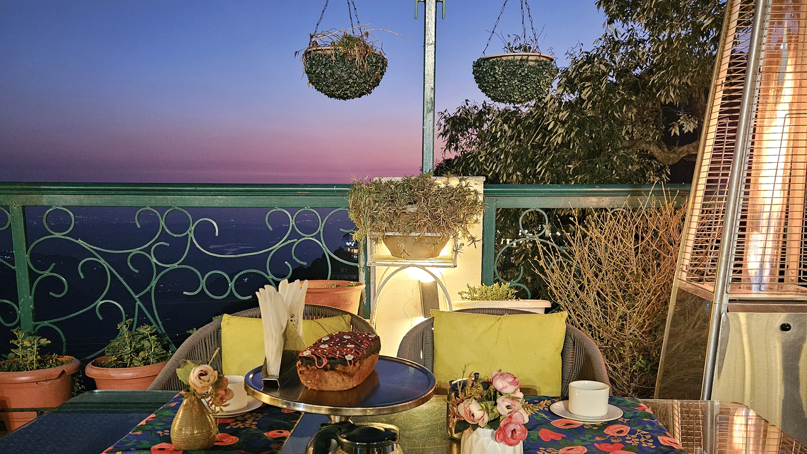 A terrace with tables set for dining under ambient lighting, offering sunset views at Mongas Hotel & Resort, Dalhousie.