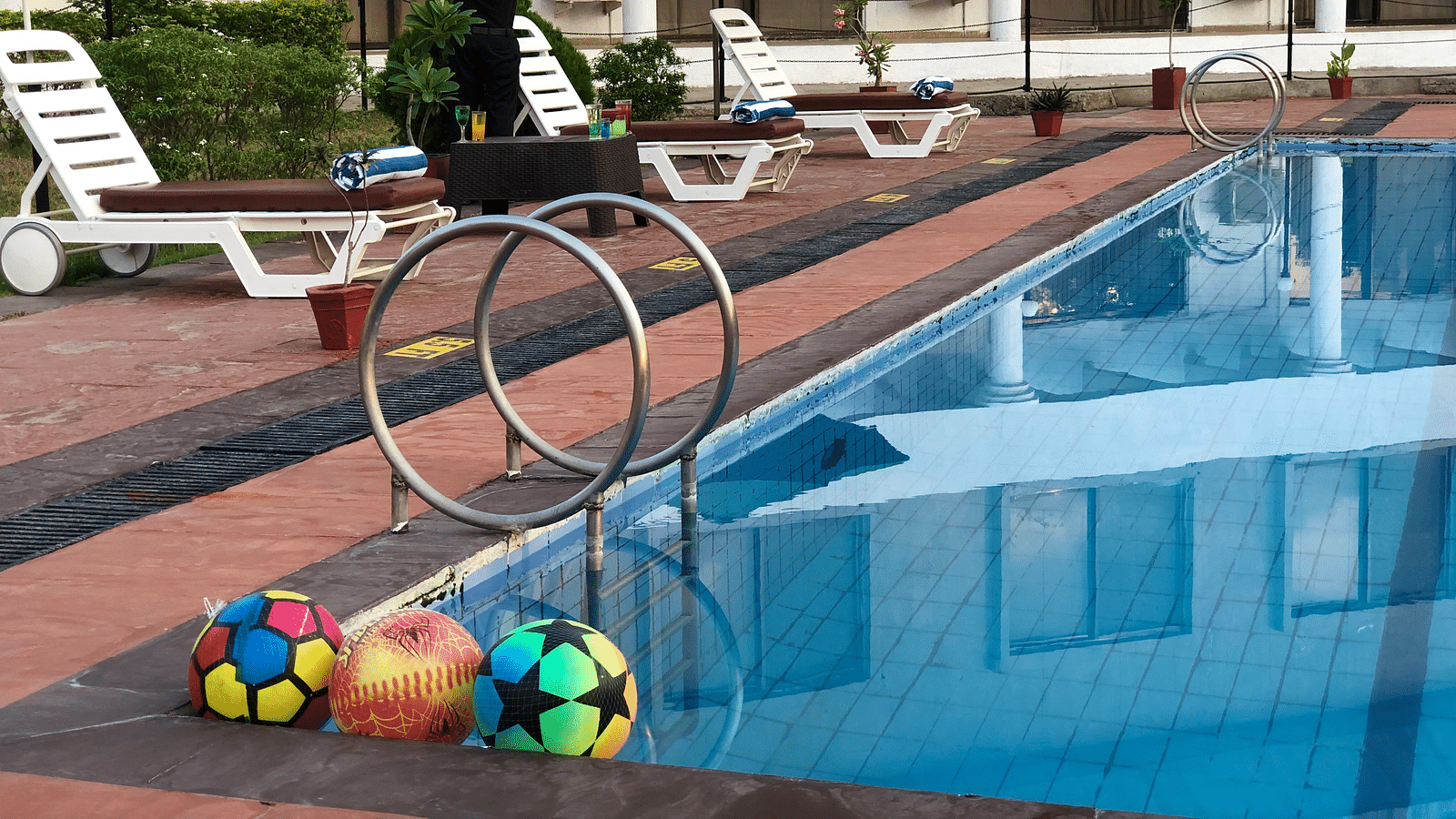 An image of a swimming pool with some water toys, and lounger placed on the side of the pool - Kamats India