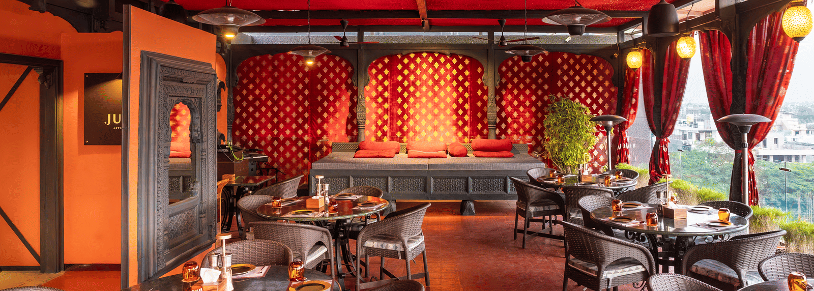 A restaurant interior with red ceiling, patterned walls, and dining tables with chairs at Infiniti Hotel, Indore.
