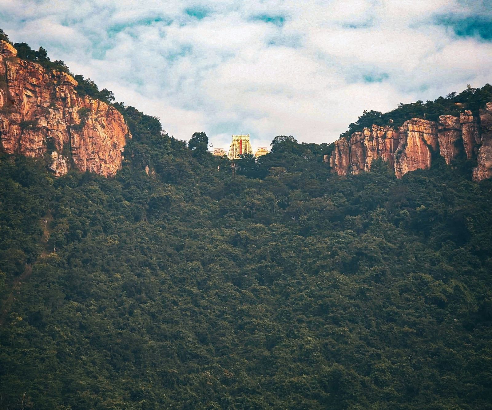 A temple nestled atop a mountain with forest cover in view 