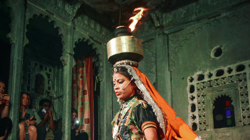 A Rajasthani folk dancer in a vibrant blue dress performing a traditional dance with a fire lamp during cultural celebrations.
