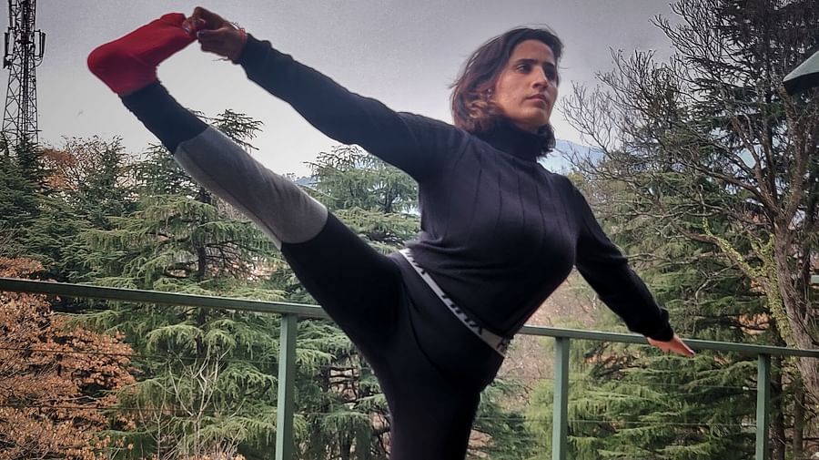 A woman doing a balancing yoga pose outdoors with a mountainous backdrop.