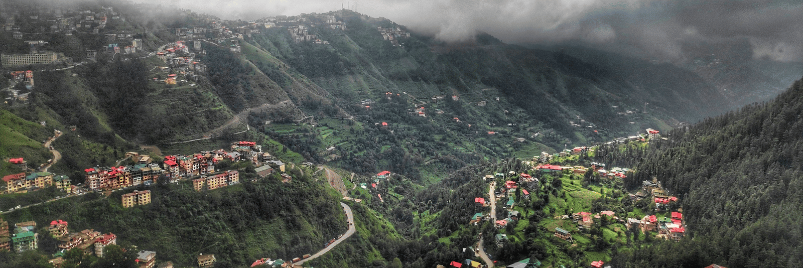 A small village with houses clustered on a hillside is shrouded in a misty, cloudy landscape.