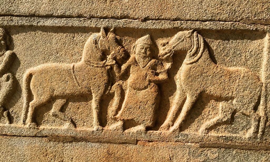 Stone carving of a man with two horses at Hampi.