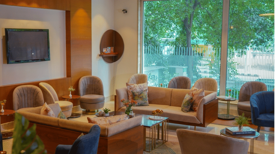 Warm and stylish lounge area with plush seating, TV, and large window views at Hotel Saket 27, New Delhi.