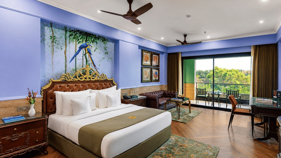 A spacious bedroom with a plush bed and a balcony facing lush greenery in a Premium Room at MAYFAIR Bay Resort, Paradeep.