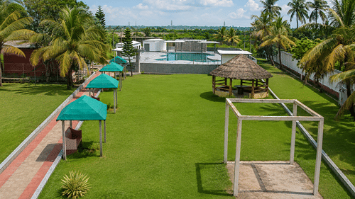 Elevated view of the lawn and rooftop pool at Pride Elite Mandarmani with a thatched gazebo, teal canopy seating, and tall palms on either side.