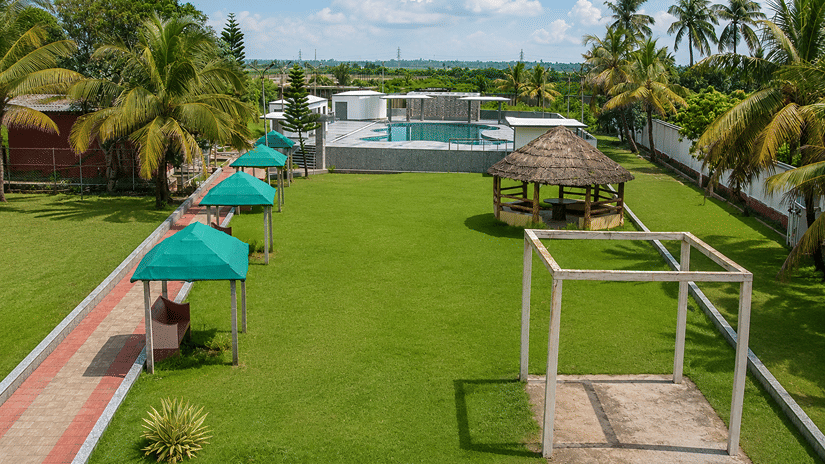 Elevated view of the lawn and rooftop pool at Pride Elite Mandarmani with a thatched gazebo, teal canopy seating, and tall palms on either side.
