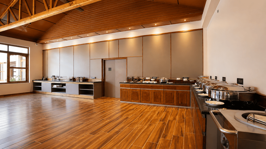The buffet counter area of the dining room at Summit Rungkhung Village Resort - The Signature Collection shows serving stations, counter space, wooden flooring, wall lamps and exposed ceiling rafters.