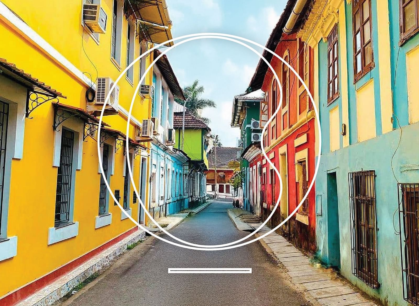 A wide angle shot of an alley in Goa with vibrant coloured buildings during a bright sunny day.