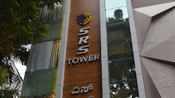Full view of the building of SRS Suites, Koramangala, surrounded by lush green trees.