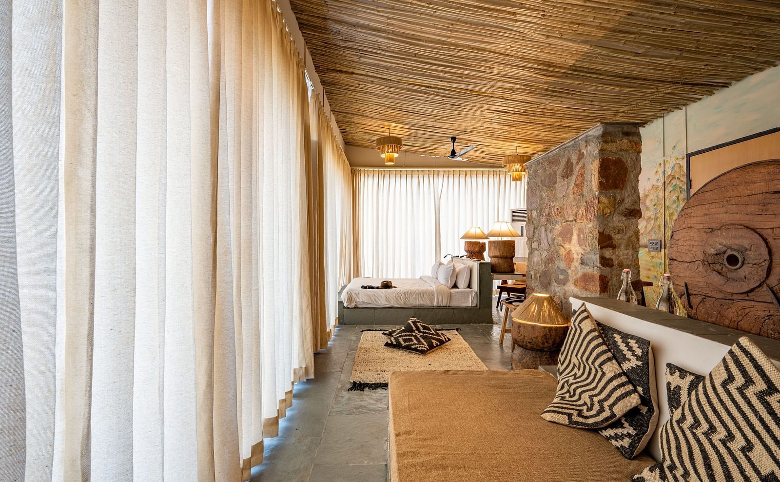An image of a room with a queen size bed, a couch, ceiling fan, chandeliers, decorative items, and wall paintings - Utsav Camp Sariska