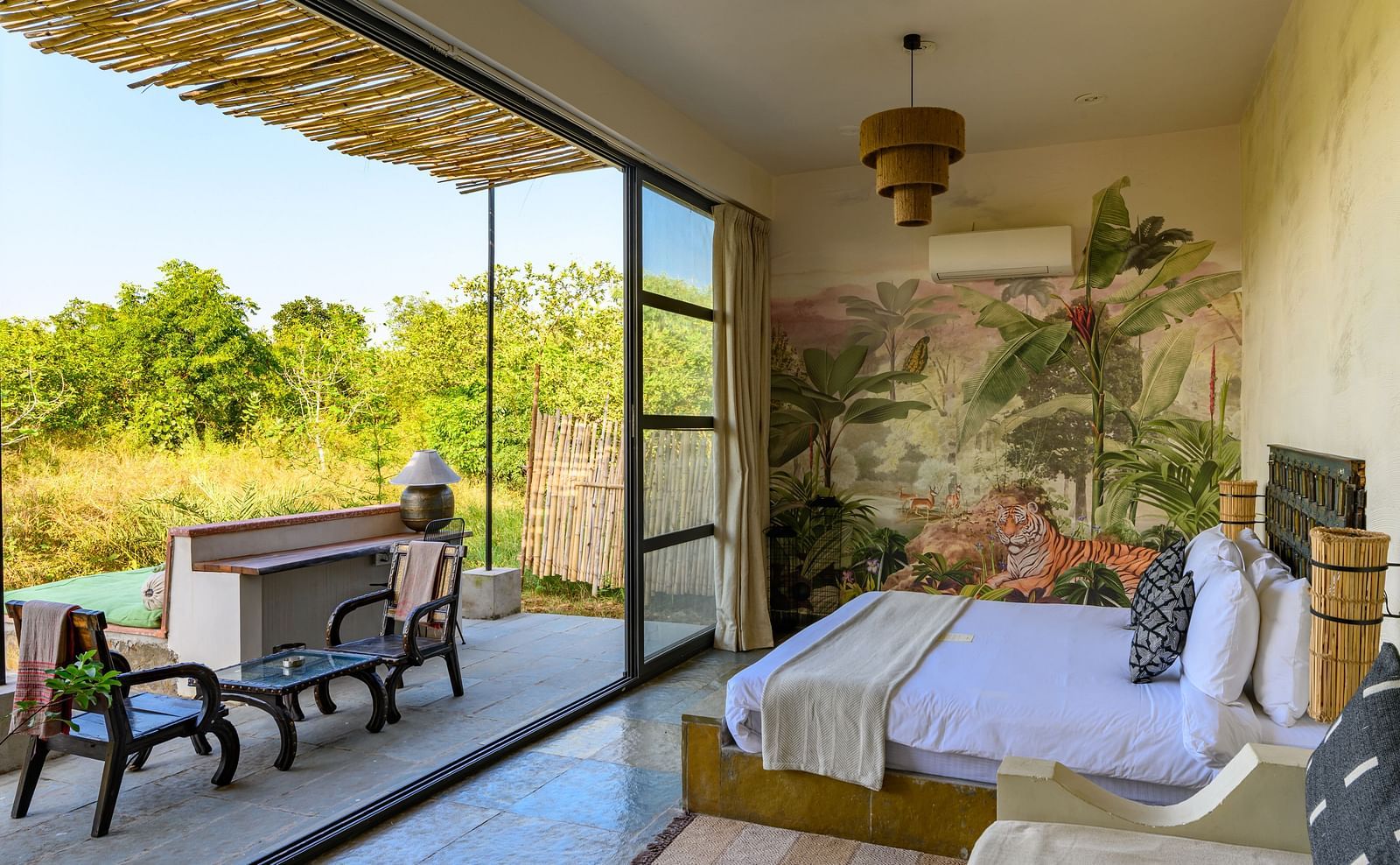 An image of a room with a queen size bed and decorative items with wall hangings and an expansive glass door with an outdoor seating arrangement - Utsav Camp Sariska