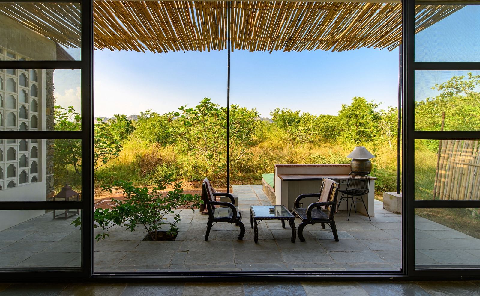 An image of an outdoor seating over looked from an expansive glass door - Utsav Camp Sariska