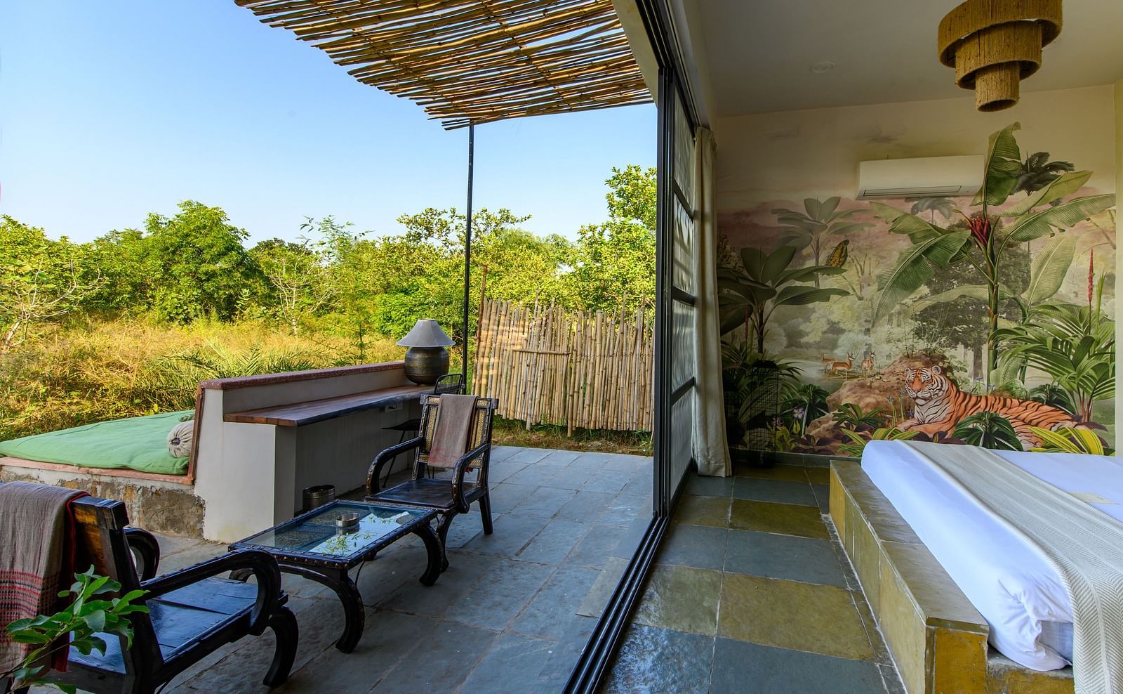 An image of a room with a queen size bed and decorative items with wall hangings and an expansive glass door with an outdoor seating arrangement - Utsav Camp Sariska