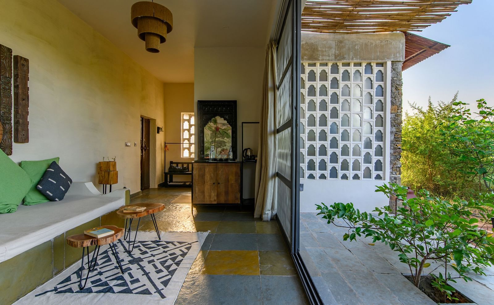 An image of a room with a queen size bed, chandelier, ceiling fan, other decorative items and an expansive glass door leading out - Utsav Camp Sariska