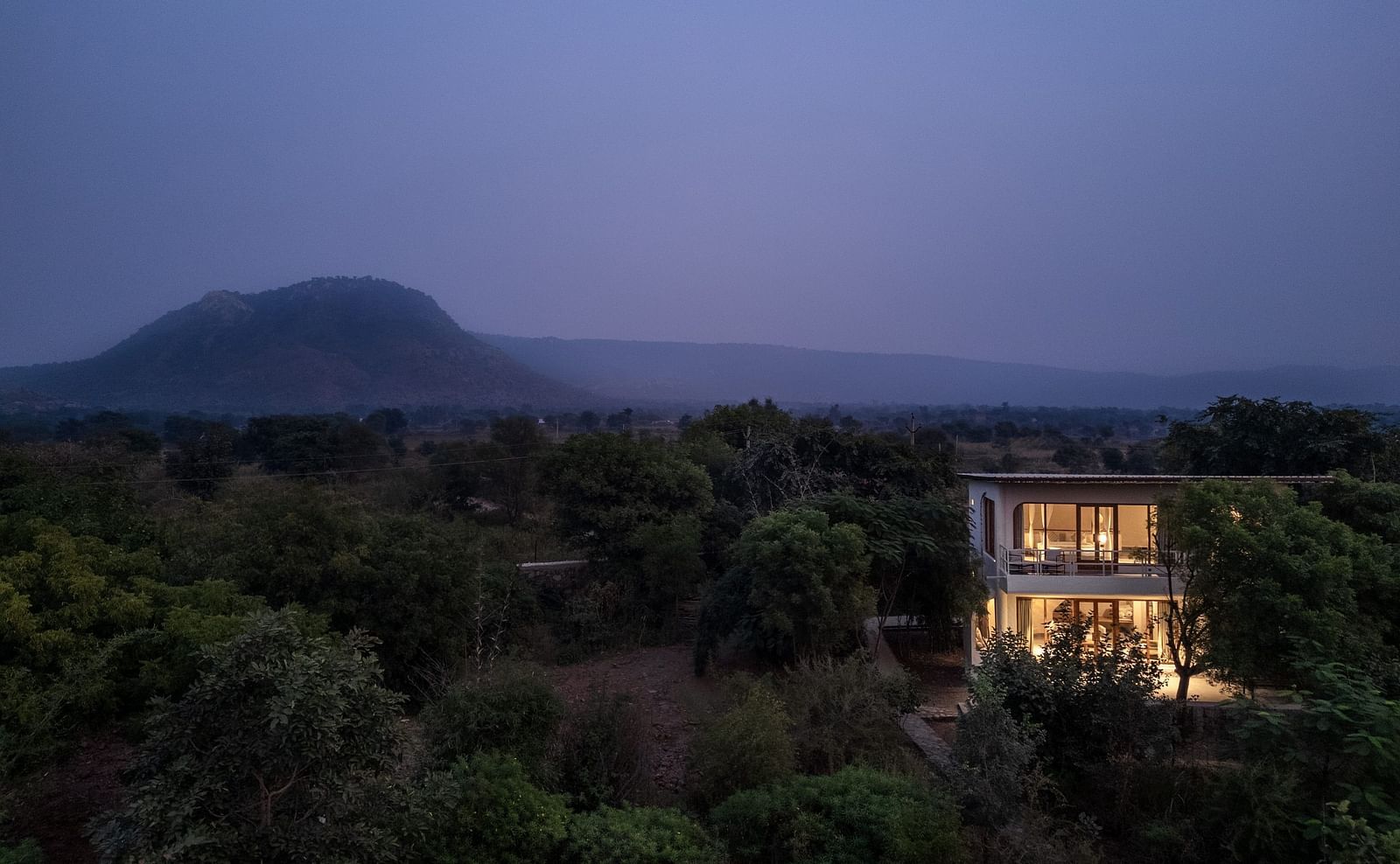 Exterior of a modern two-story villa surrounded by trees and plants.