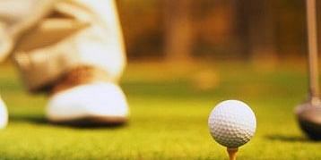 a golf ball on a tee with a persons leg in the background at a golf course - Caravela Beach resort