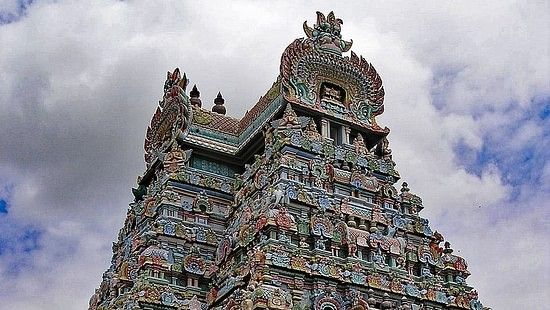 A tall, intricately sculpted temple tower with colourful figures against a cloudy sky.