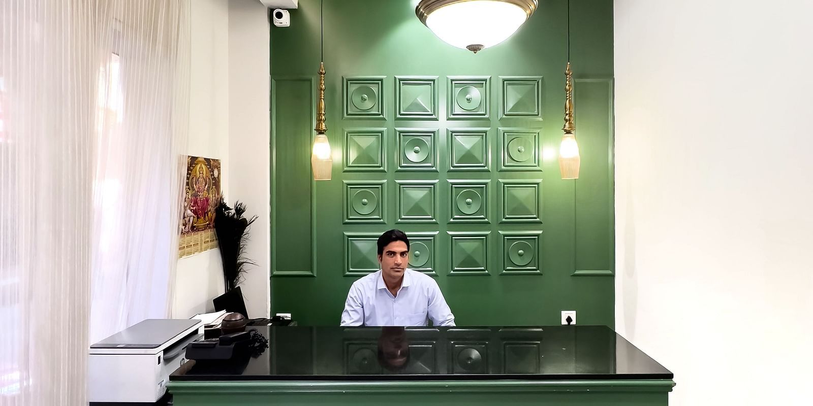 A hotel reception area with a green desk and a person sitting behind it - Wonder Hills
