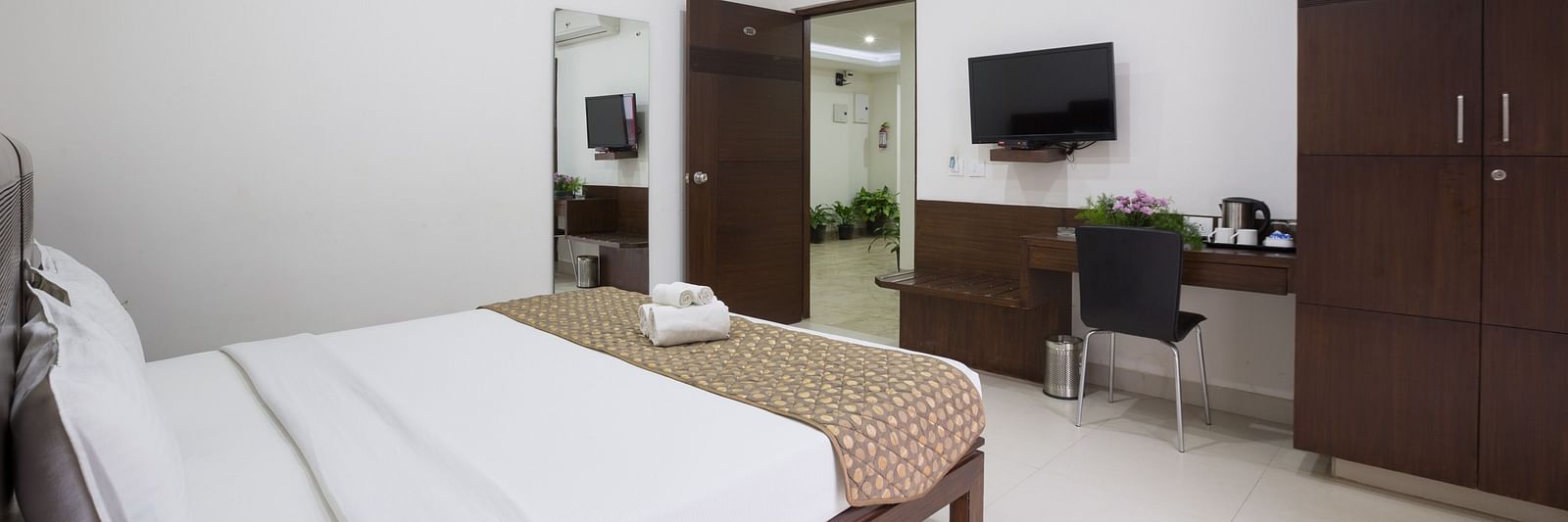 A room with a bed, a desk area, wardrobe, and a television mounted on the wall - Sanctum Suites BEL Road, Bangalore