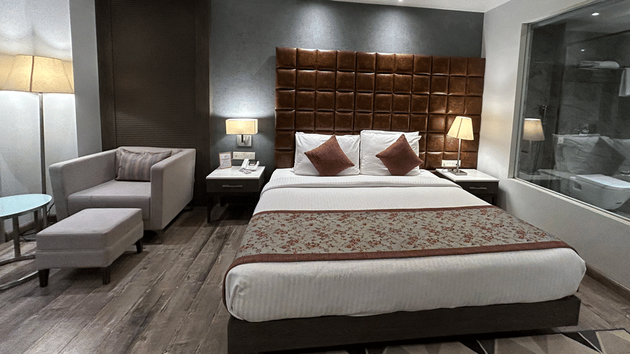 A bedroom featuring a double bed, a grey armchair with a footstool, and a large window