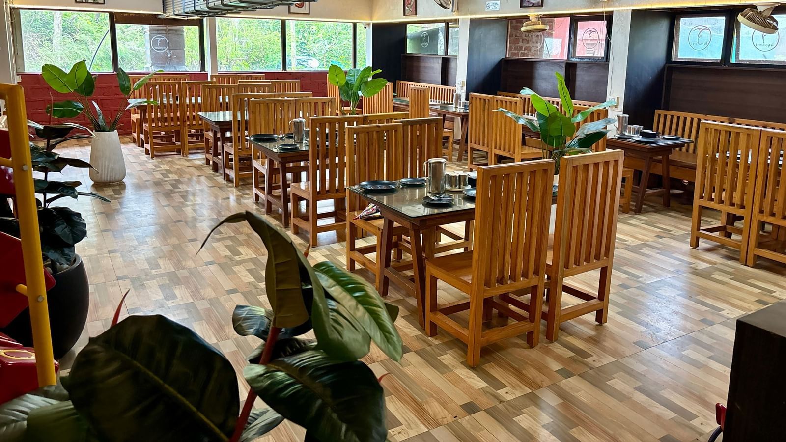 An empty dining area with simple wooden tables and chairs, and large potted plants placed throughout the room - Tranquil Beach Resort, Harihareshwar