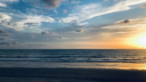 Orange sun setting over a calm ocean with blue sky and clouds.