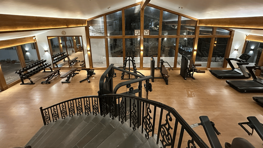 A gym floor with treadmills, elliptical machines, stationary bikes, and a curved staircase overlooking the workout area at Clarks Avadh, Lucknow.