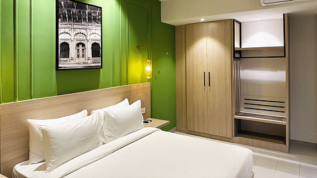 A close up shot of a hotel room with a large white bed placed under a vintage painting attached to a green coloured wall - Wonder Hills