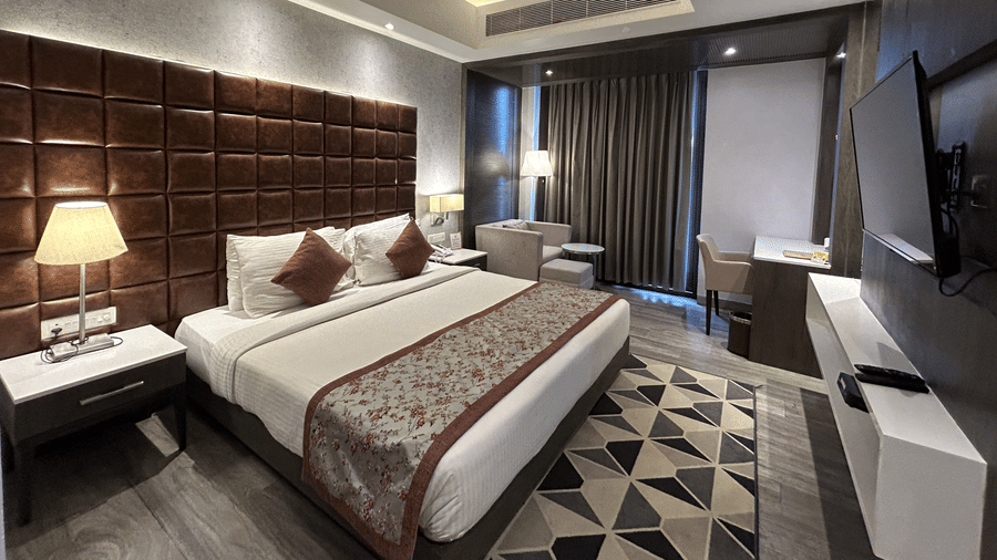 A hotel bedroom featuring a bed with a brown padded headboard, a bedside lamp, and a television