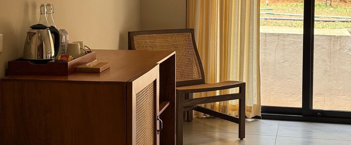  A hotel room interior featuring a wooden cabinet with a kettle, a chair, and a large sliding glass door leading to a balcony.