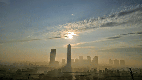 a far out view of Gurgaon with the sky line dotted with skyscrapers and the sun in the background.