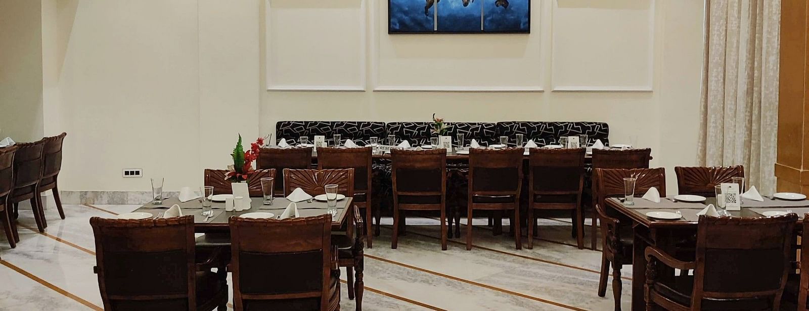 A brightly lit dining area of Gold Plate restaurant with tables and chairs neatly arranged along with a chandelier hanging from the ceiling - Hotel Gold, Panipat