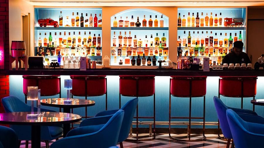 Modern bar interior with vibrant lighting highlighting a full array of spirits on shelves, sleek bar stools, and a reflective tile floor.