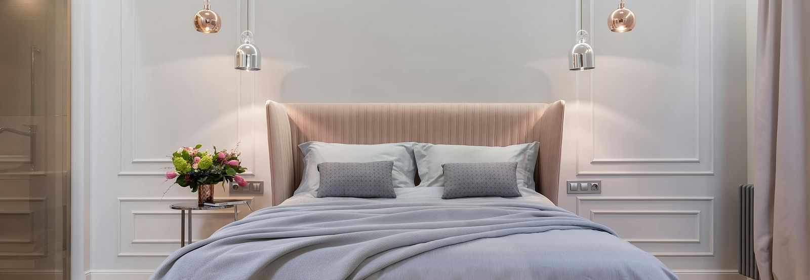 A modern bedroom is shown with soft lighting, a grey duvet, and a tufted bench.
