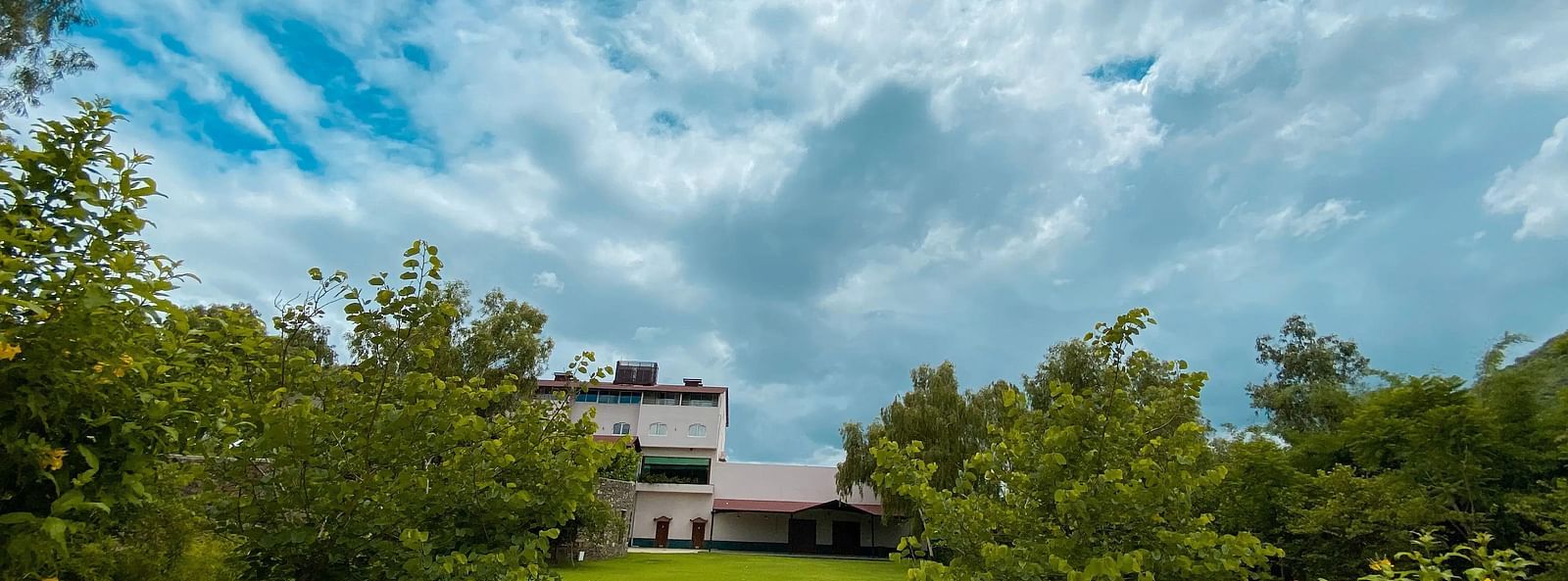 Green garden with trees and buildings under a cloudy sky.