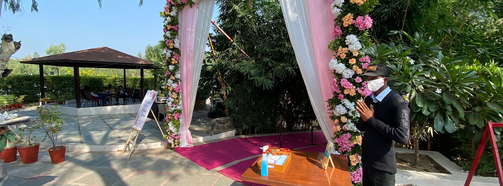 Arched floral decor, wooden table, stone path, green trees.