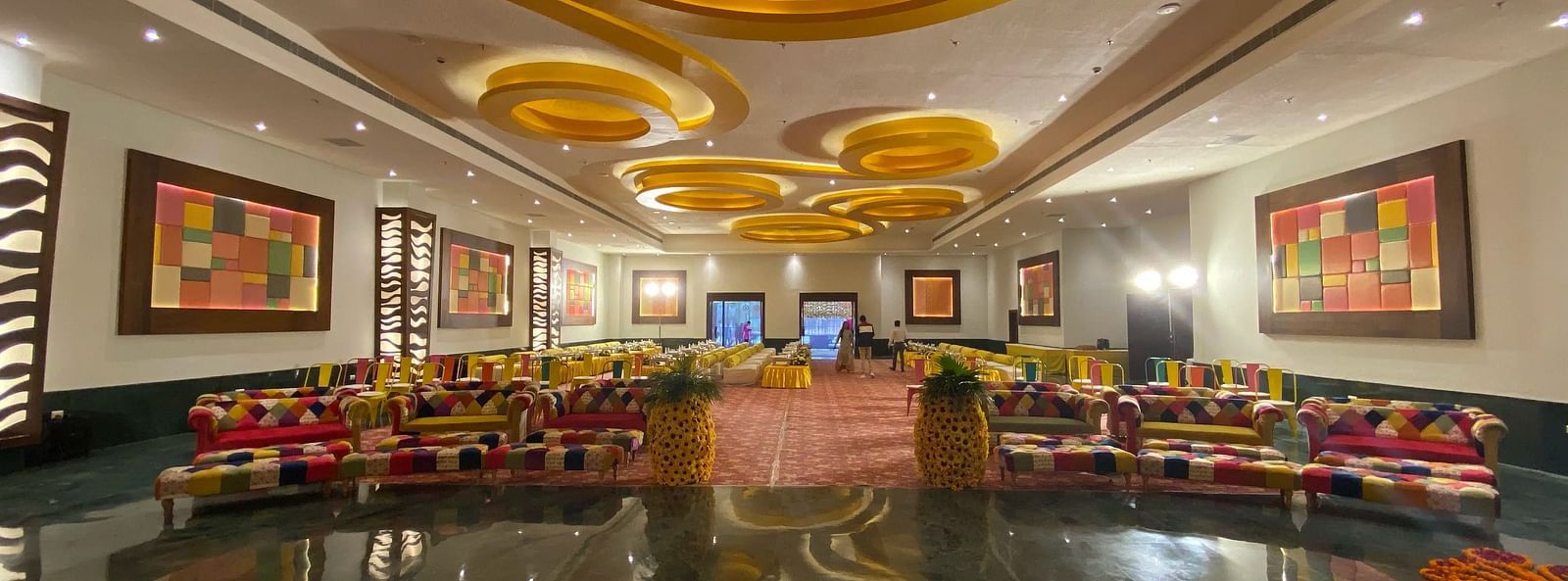 A large indoor hall with patterned carpet, gold ceiling, and artwork framed in the wall.