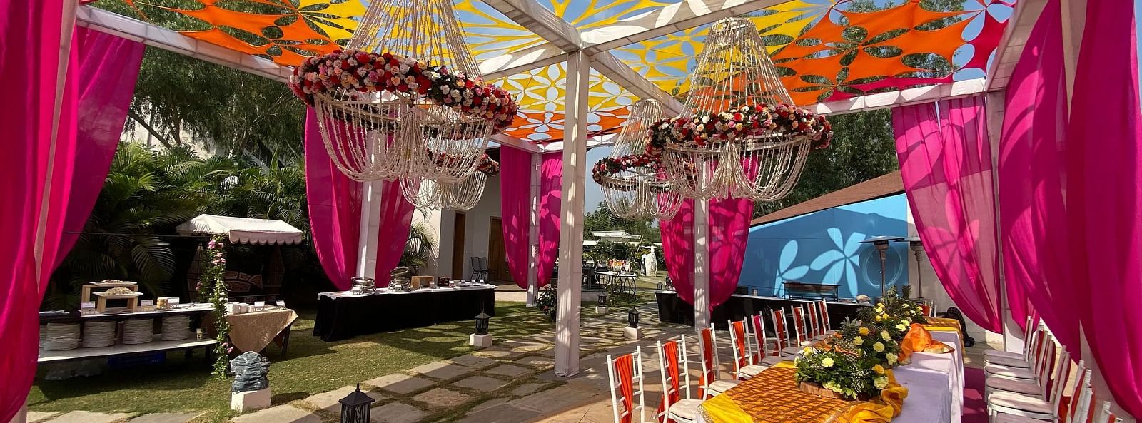 Tent with colourful fabric ceiling, drapes, and set tables.